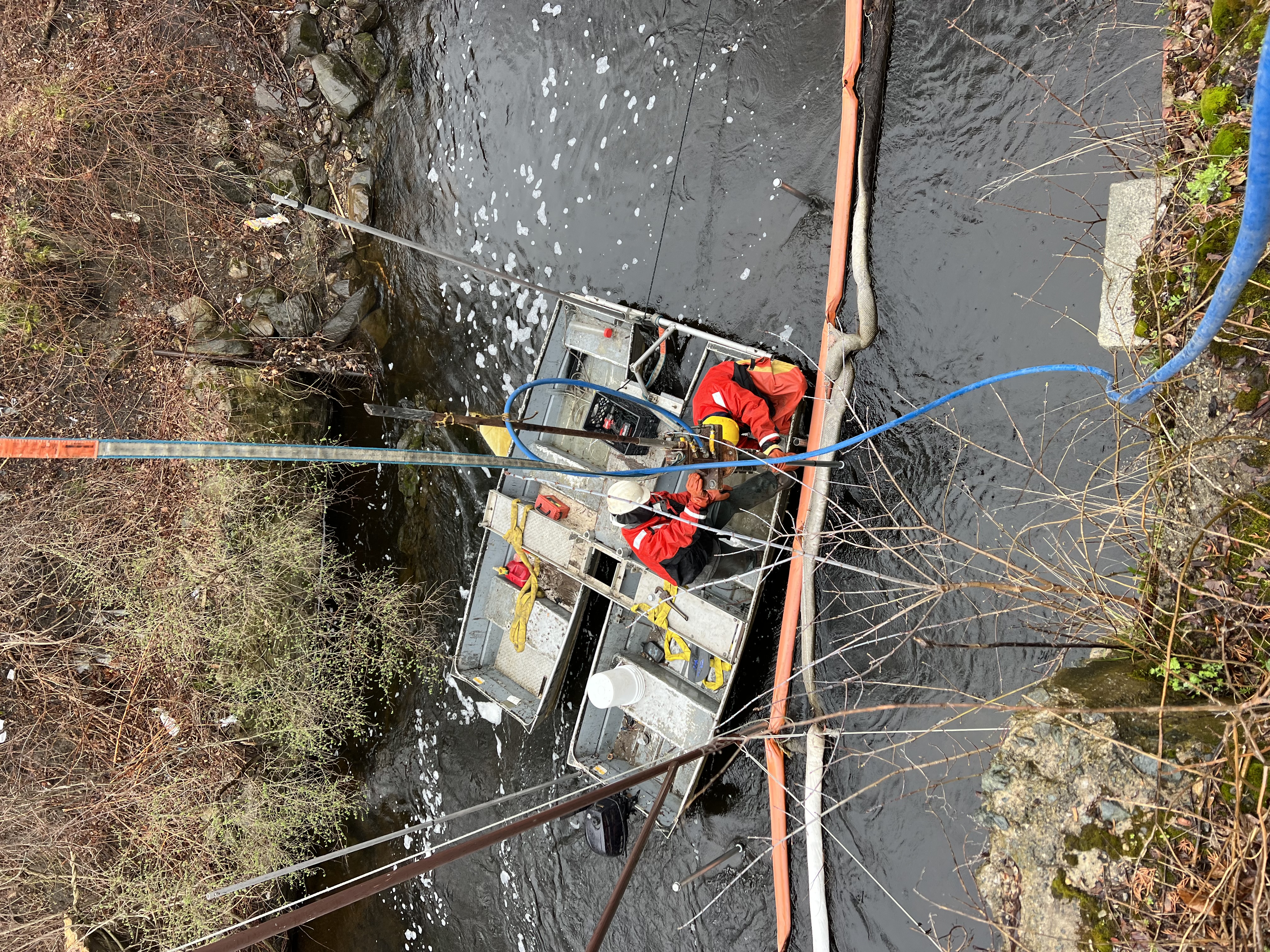 Workers operating vibracore in an urban creek during remediation sampling